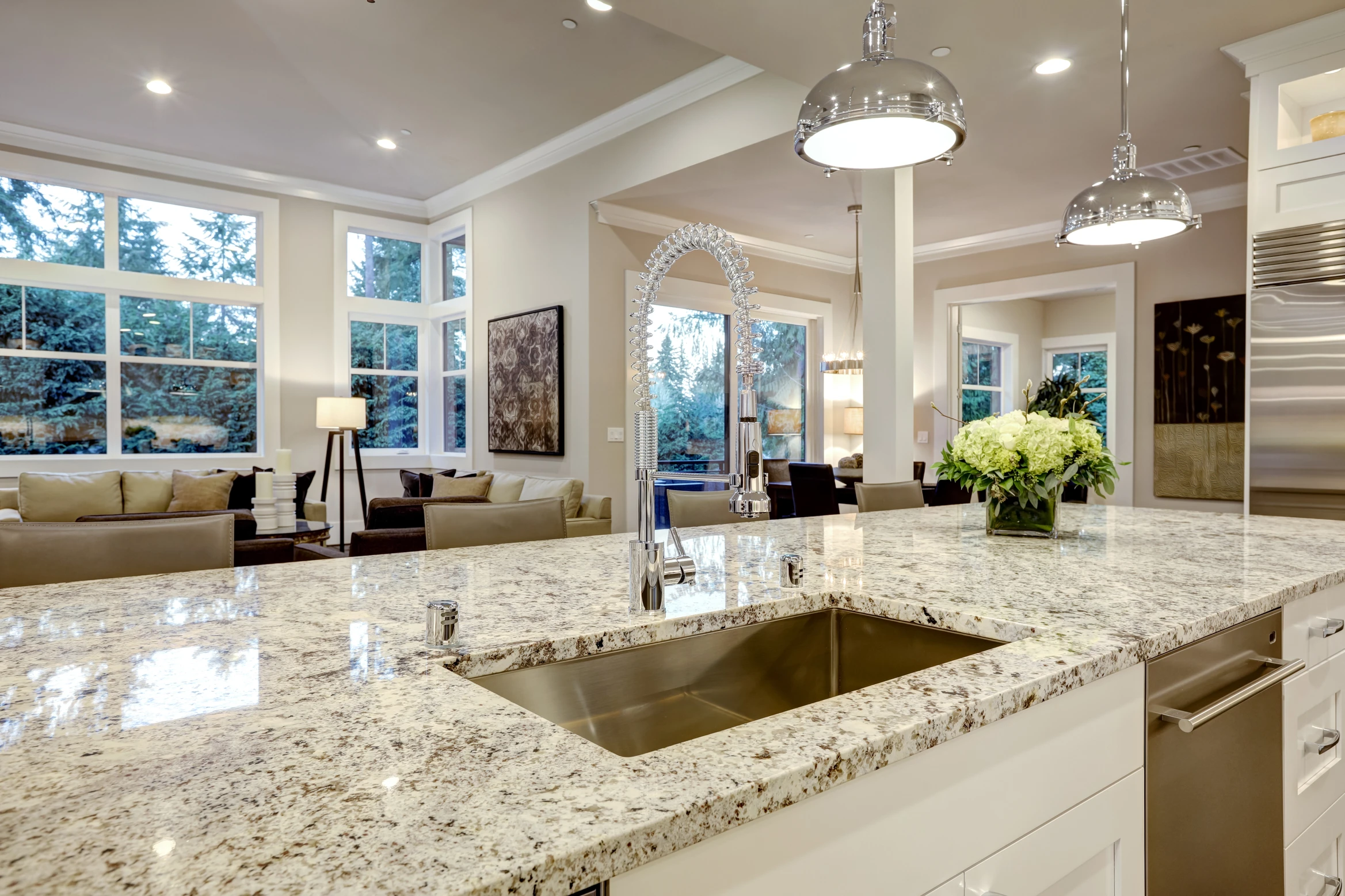 Modern kitchen with granite countertop, functional islands, stainless sink, pendant lights, open to bright living area.