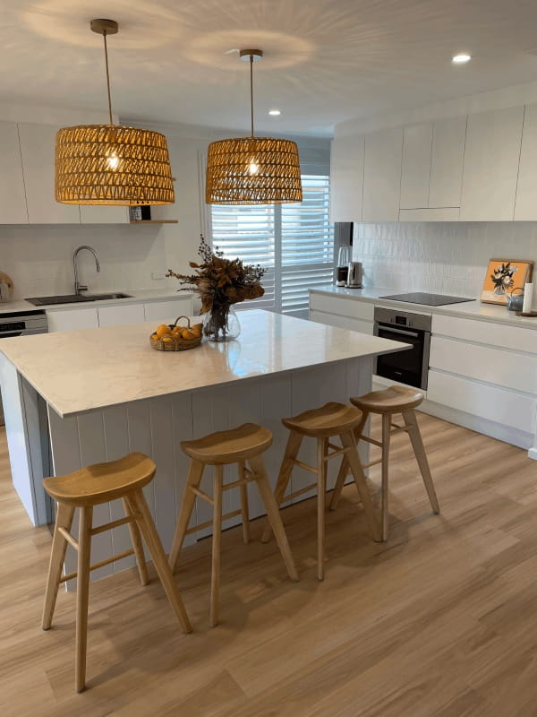 Modern cromer kitchen with white cabinets, marble island, four stools, pendant lights, and flowers. Red Hot Kitchens style.