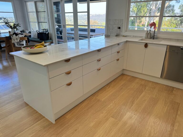 Modern kitchen with Collaroy Plateau — Door & Benchtop Reface, white cabinets, wood floors, dining and trees view.