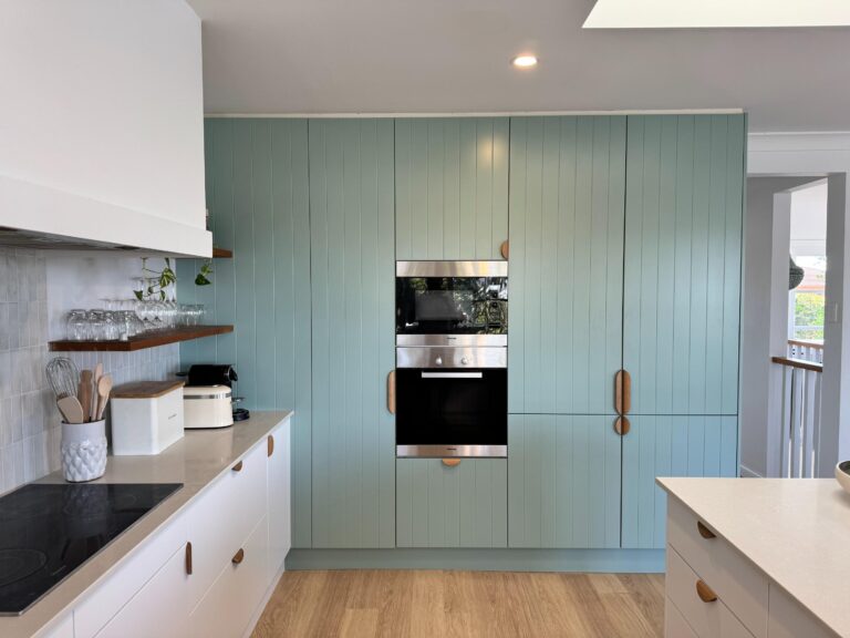 Modern kitchen with light blue vertical cabinets, white countertops, wood accents & natural light; Collaroy Plateau reface.
