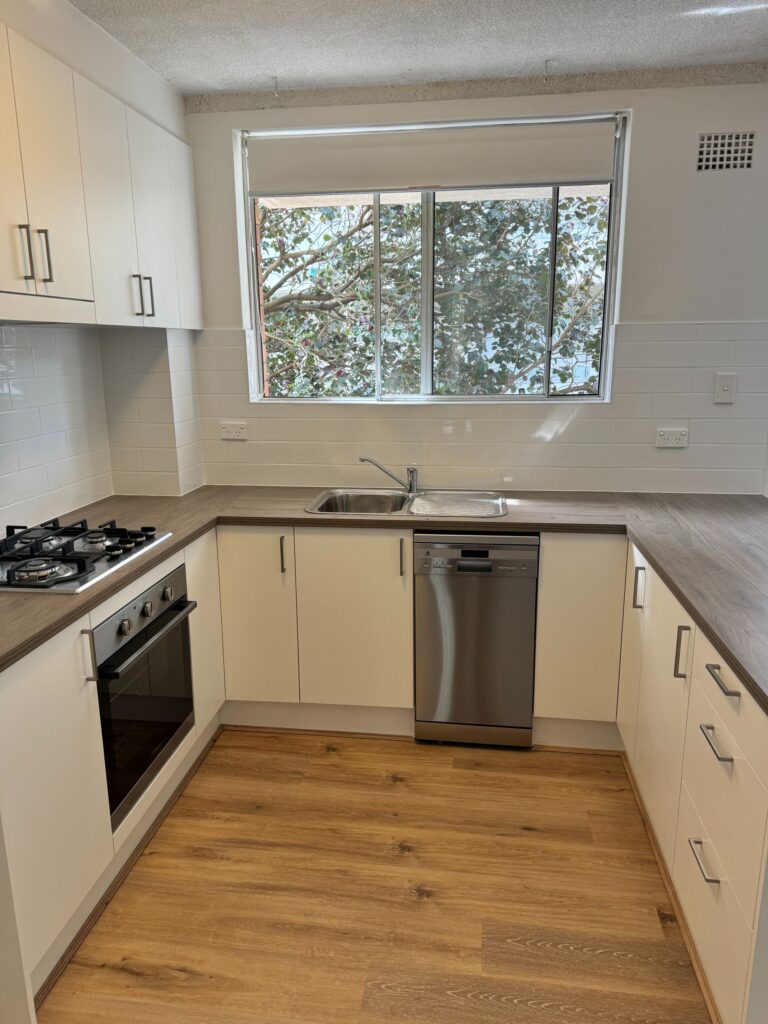 Modern kitchen with white cabinets, Door Reface, stainless appliances, gas stove, dishwasher, and large sunlit window.