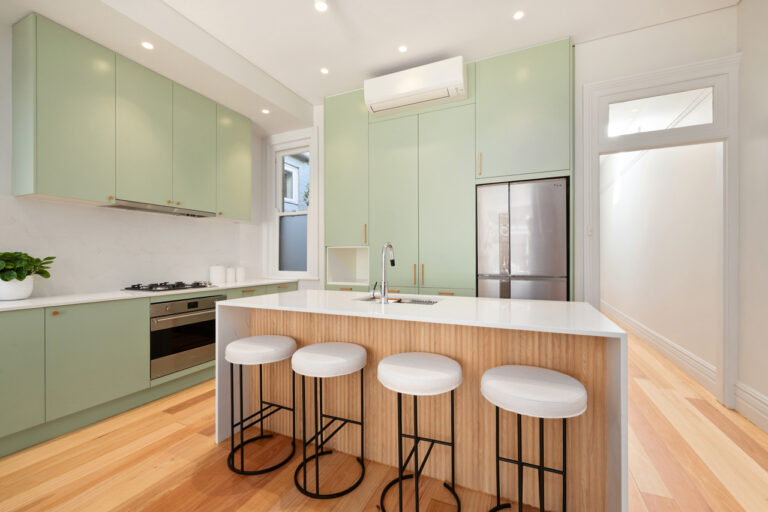 Modern kitchen with mint green cabinets, white countertops, wood accents, and stainless steel appliances—refreshed by Manly Door & Benchtop Reface.