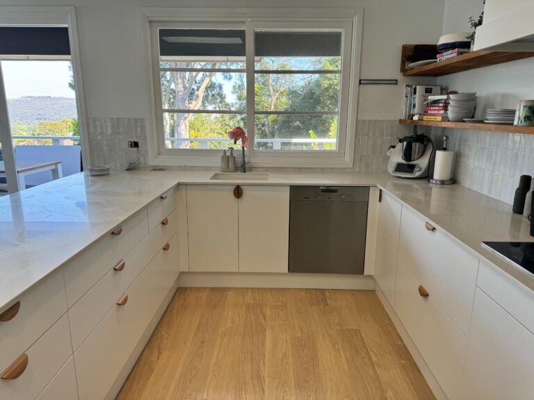 Modern kitchen with white cabinets, wooden handles, light countertops, a stylish Collaroy Plateau Door & Benchtop Reface.