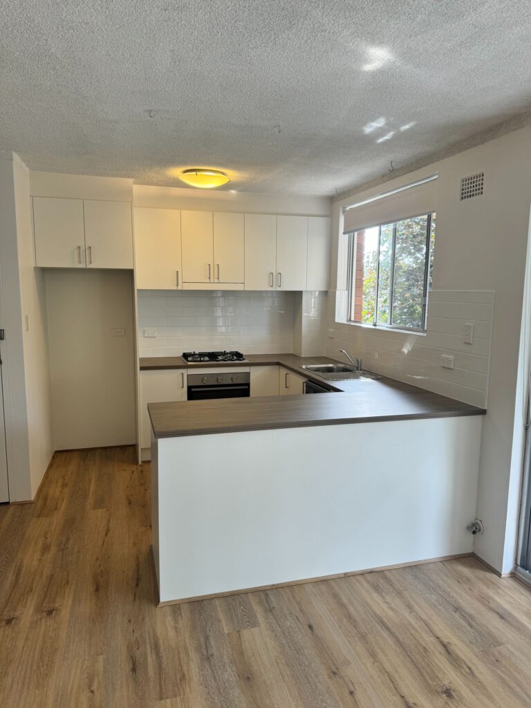 Modern kitchen with Door Reface, white cabinets, wood countertops, gas stove, oven, sink by window.