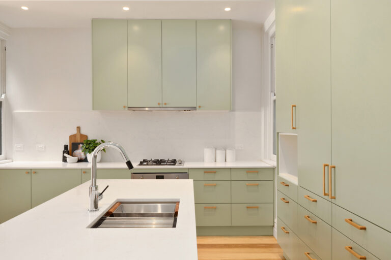 Modern kitchen with pale green cabinets, Manly — Door & Benchtop Reface, white counters, gold hardware.