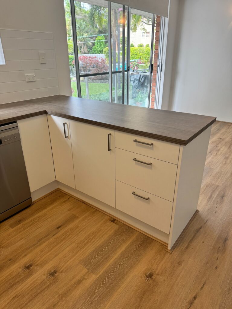 Modern kitchen with white cabinets, sleek silver handles, dark countertop, and updated door reface near sliding glass door.