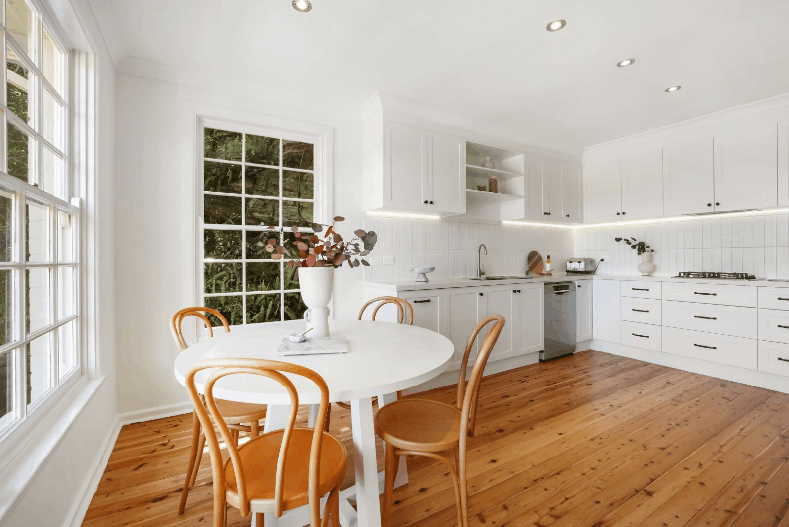 Bright, white kitchen with wood floor and round table by Red Hot Kitchens—quality materials for kitchen makeovers.