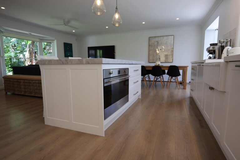 Modern kitchen by Red Hot Kitchens features white cabinets, marble island, and wood floors in Mona Vale.