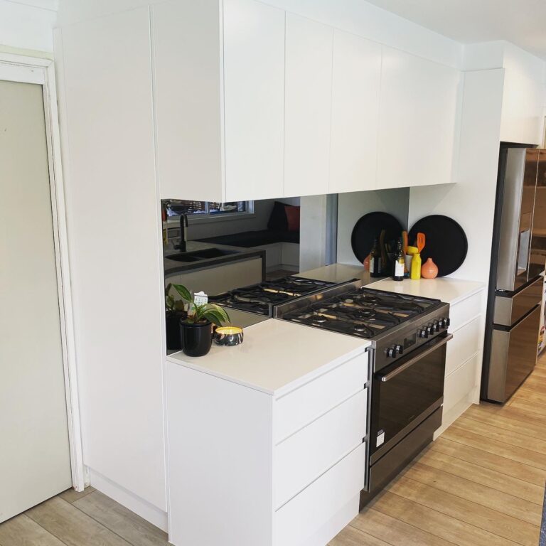 Red Hot Kitchens modern white kitchen in Wheeler Heights with sleek black stove, white cabinets, and wood floor.