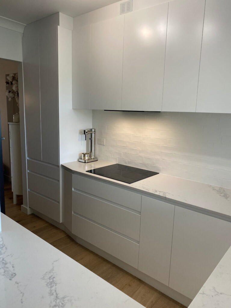 Sleek Queenscliff kitchen by Red Hot Kitchens featuring white cabinets, marble counters, and light wood flooring.