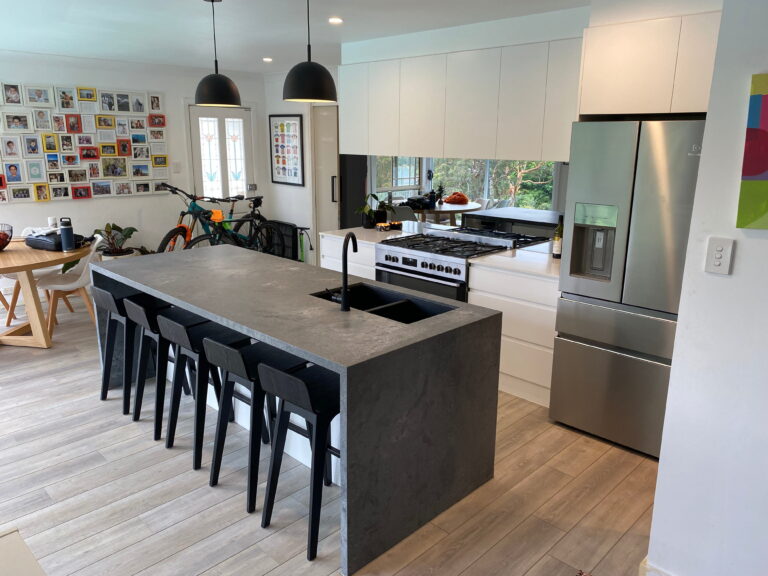 Red Hot Kitchens by Wheeler Heights: modern space with sleek dark island, black chairs, stainless appliances, photo wall.