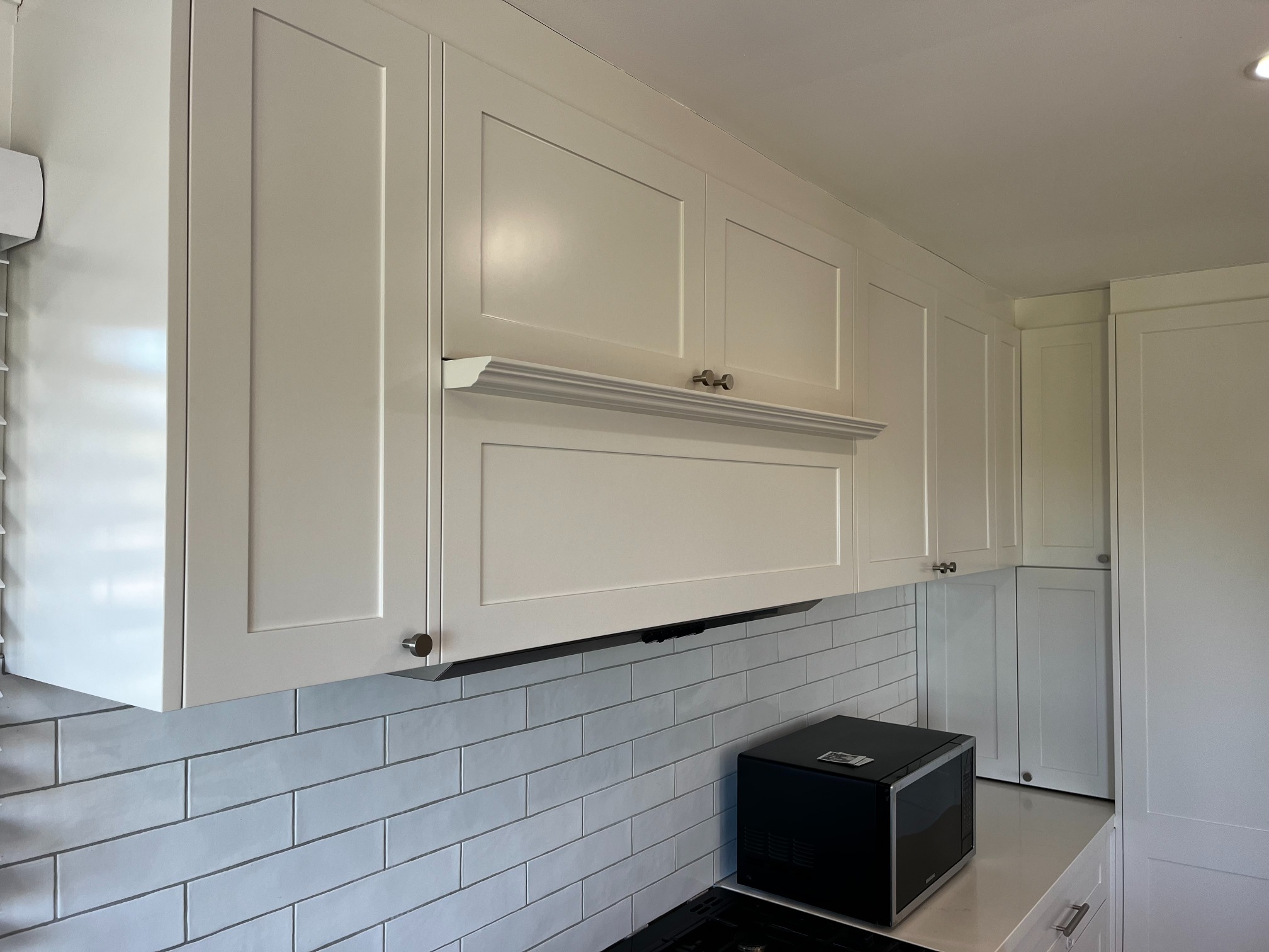 Custom Kitchens features white cabinets with silver knobs, black microwave, subway tile backsplash, and stove.