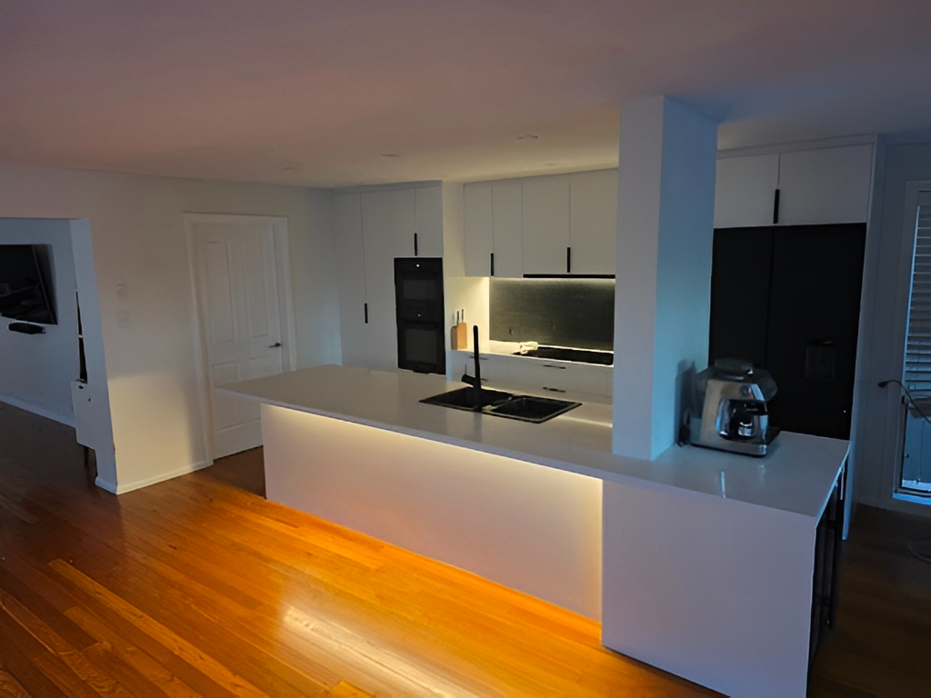 Custom modern kitchen with white cabinets, black appliances, island, and wood floor by Red Hot Kitchens.