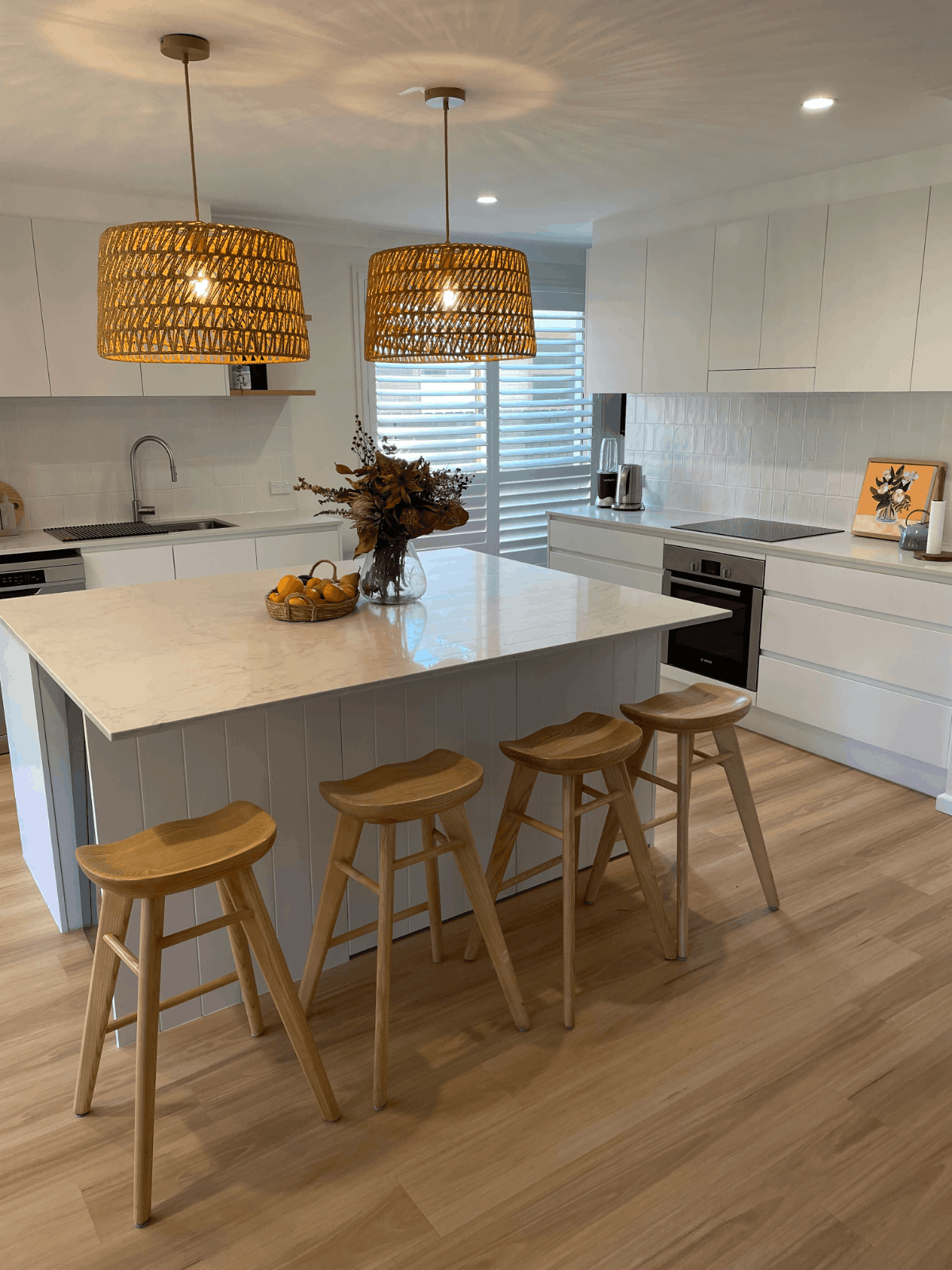 Modern kitchen renovations Northern Beaches, featuring white cabinets, large island, wood stools, and pendant lights.