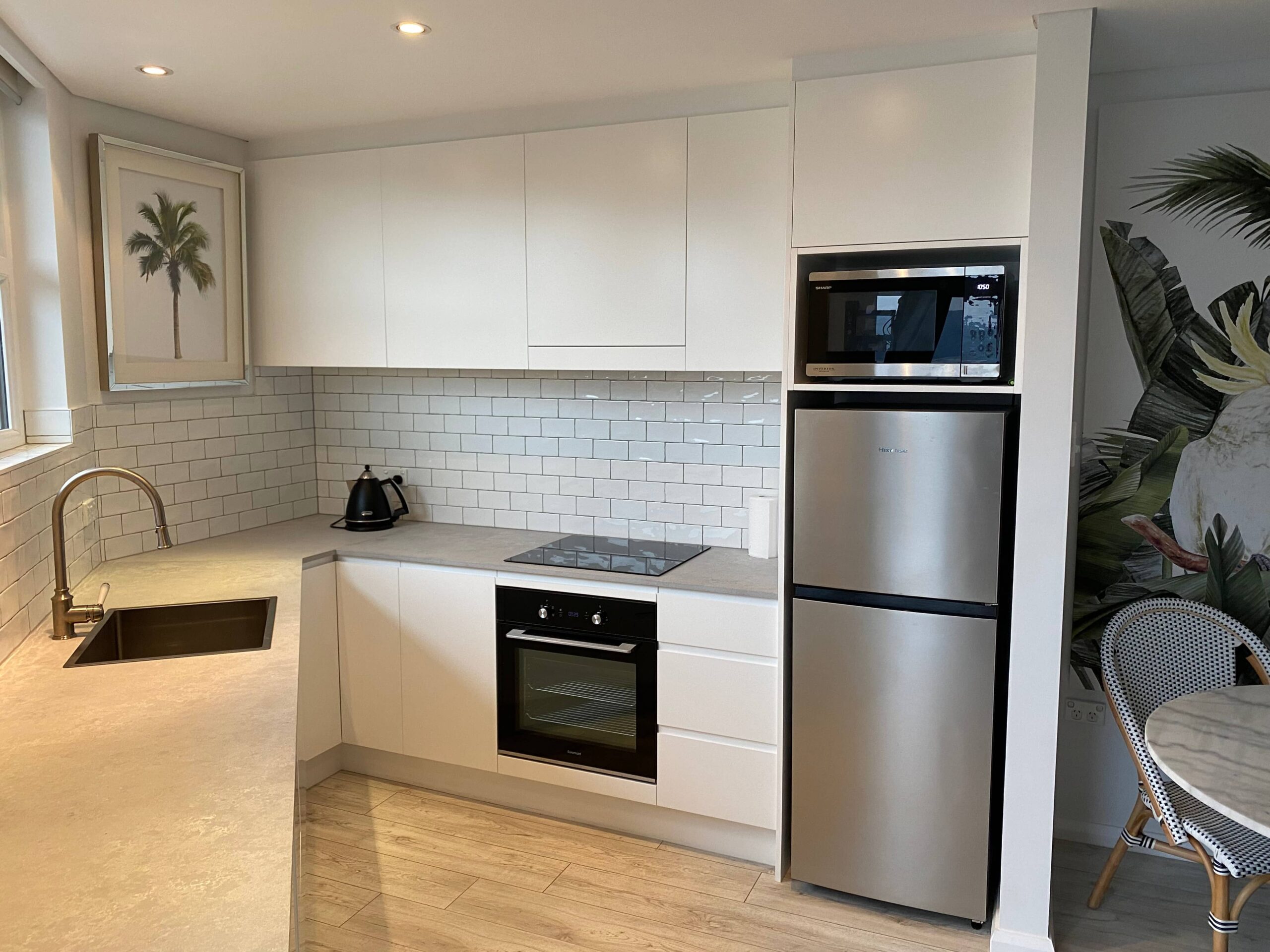 Modern kitchen renovation in Manly with white cabinets, stainless appliances, tile backsplash, and tropical mural.