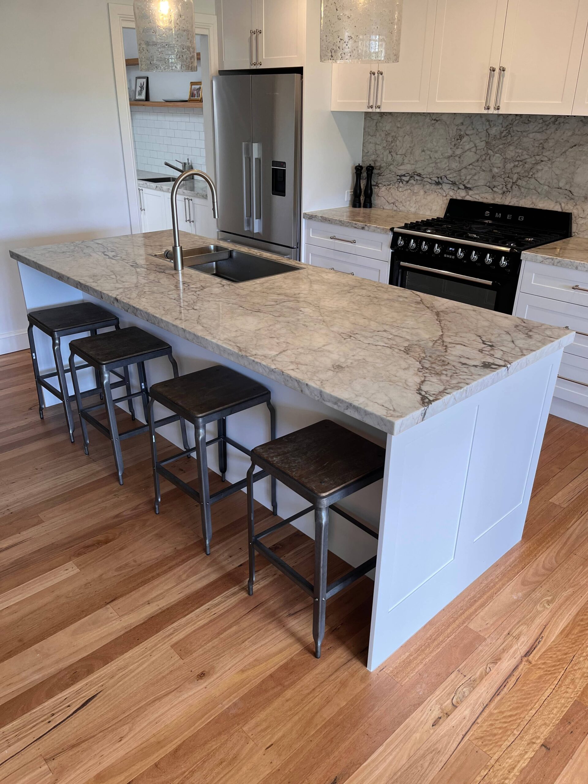 Modern kitchen with marble island, built-in sink, bar stools, stainless appliances & white cabinets—Red Hot Kitchens.