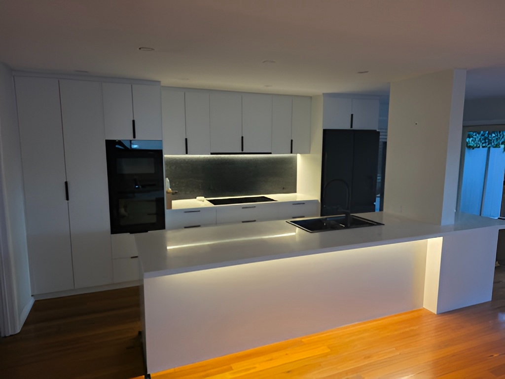 Modern kitchen by Red Hot Kitchens with white cabinets, black handles, built-ins, island & wooden floor.