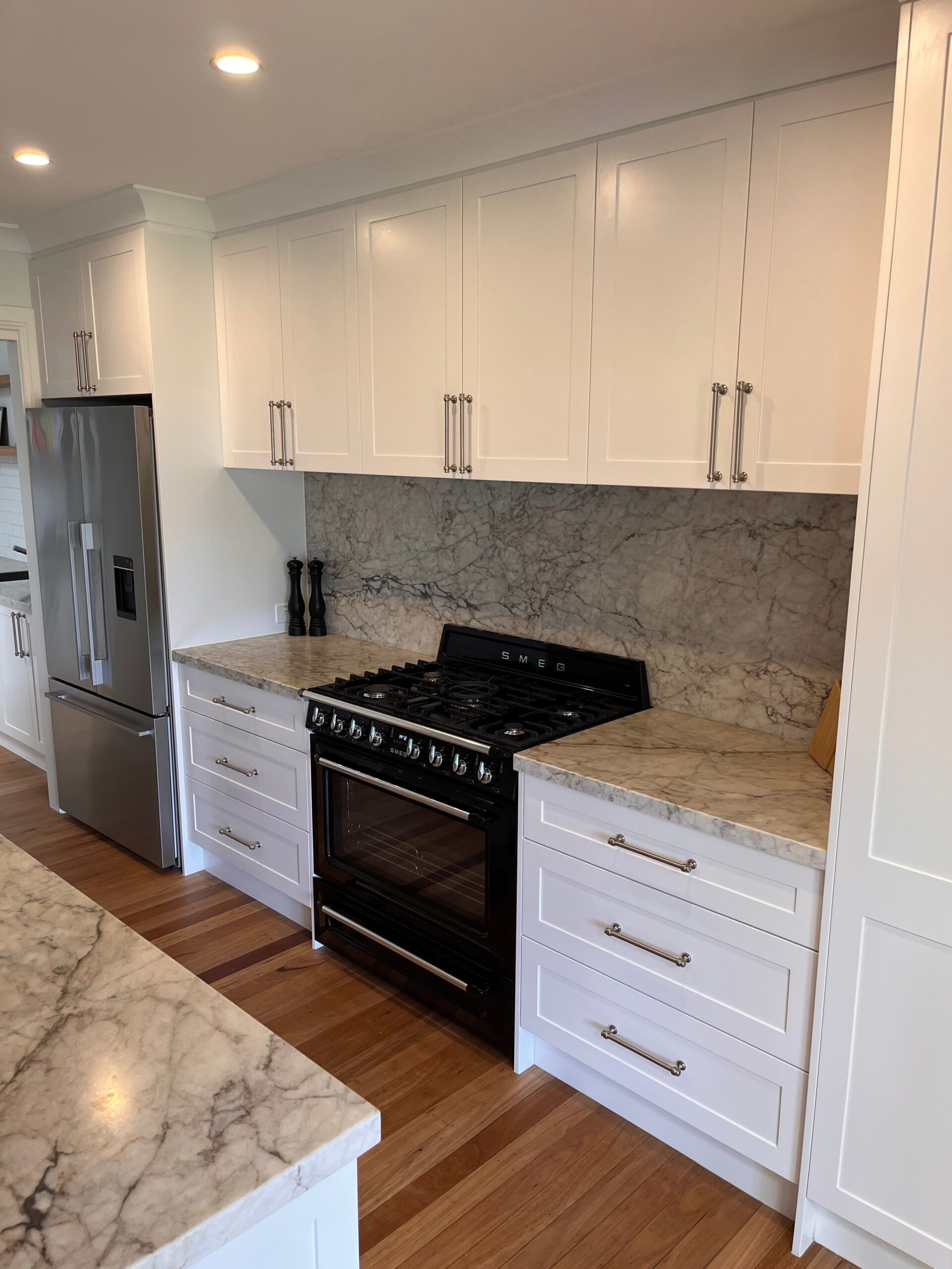 Modern kitchen renovation with white cabinets, marble counters, stainless fridge, and black gas range in Collaroy Plateau.