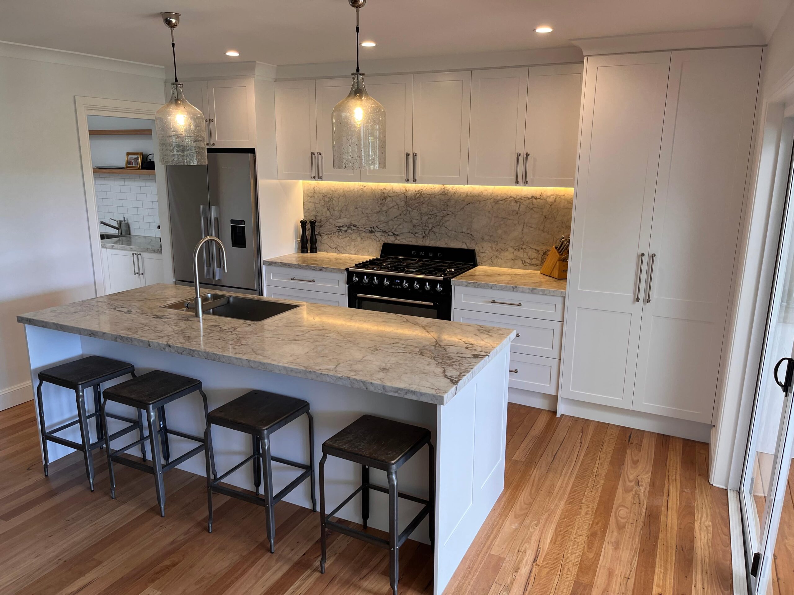 Modern kitchen renovation in Collaroy Plateau with marble island, metal stools, white cabinets, and wood floors.