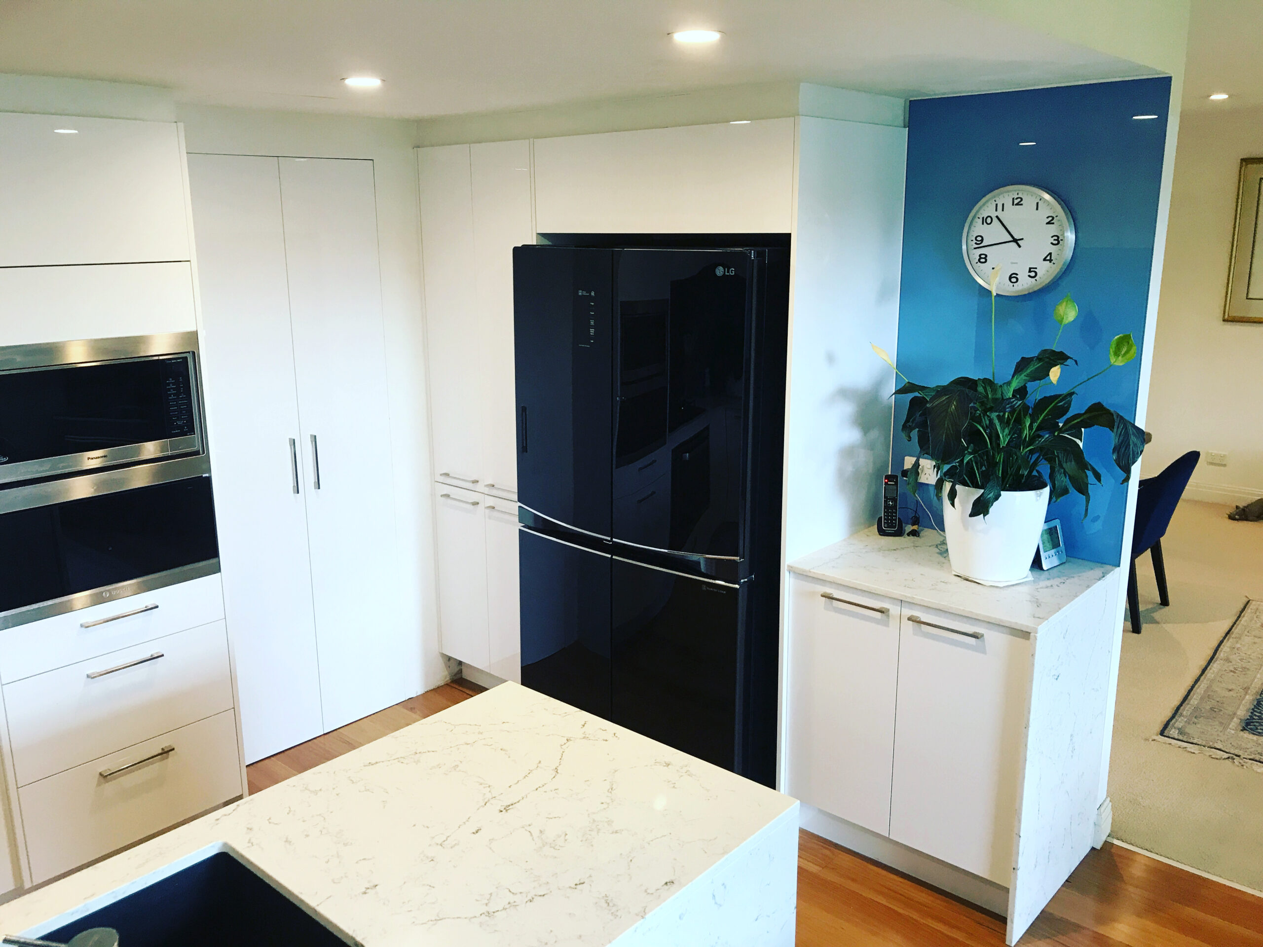 Modern kitchen with white cabinets, black fridge, built-in ovens, marble counters, plant, and blue accent wall