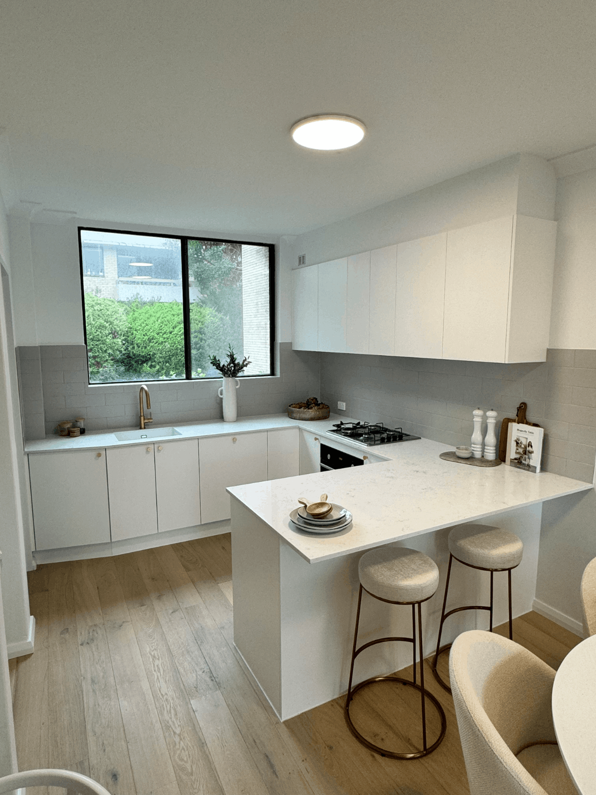 Modern kitchen with white cabinets, marble countertop, barstools, gas cooktop, large window and wood floors.