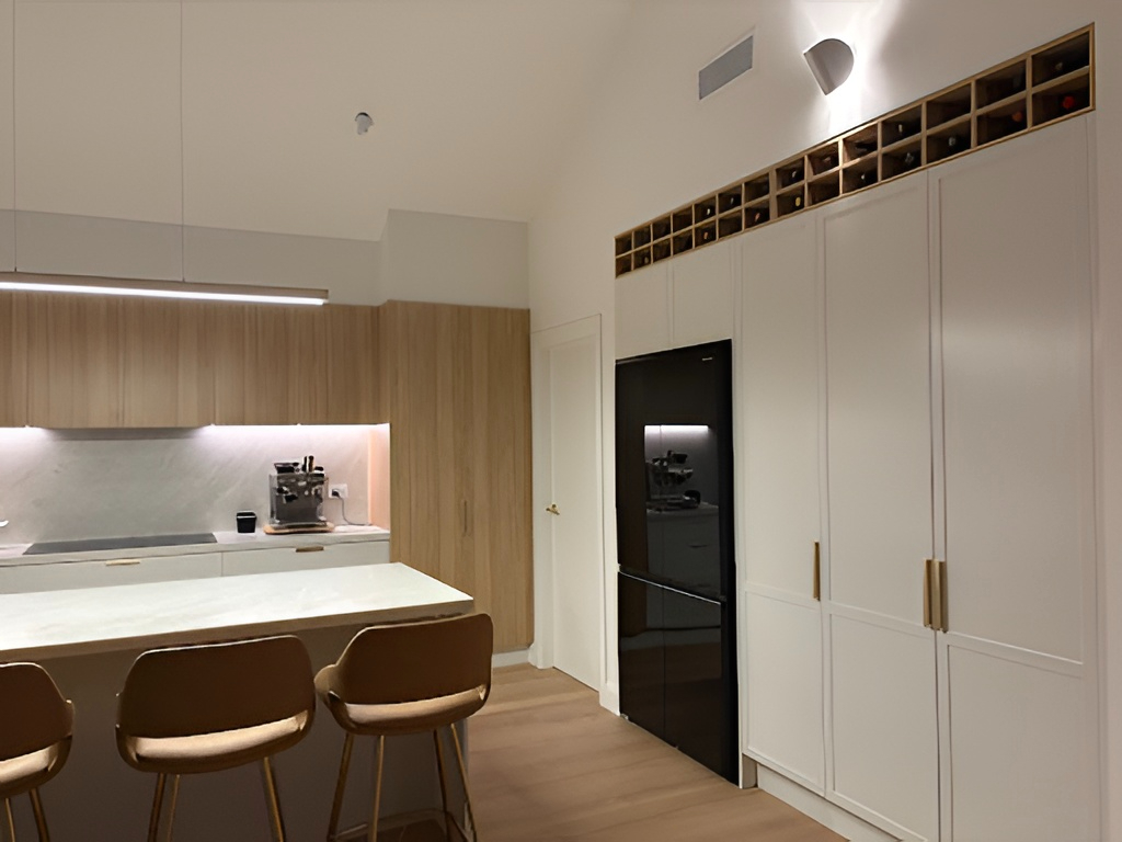 Modern kitchen in North Curl Curl with light wood cabinets, black fridge, marble counter, and wine rack. Stylish living.