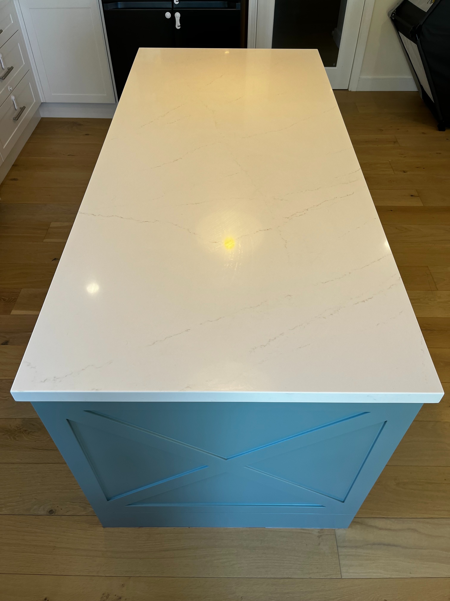 Red Hot Kitchens custom kitchen island with white marble top, blue base, and light wood flooring.