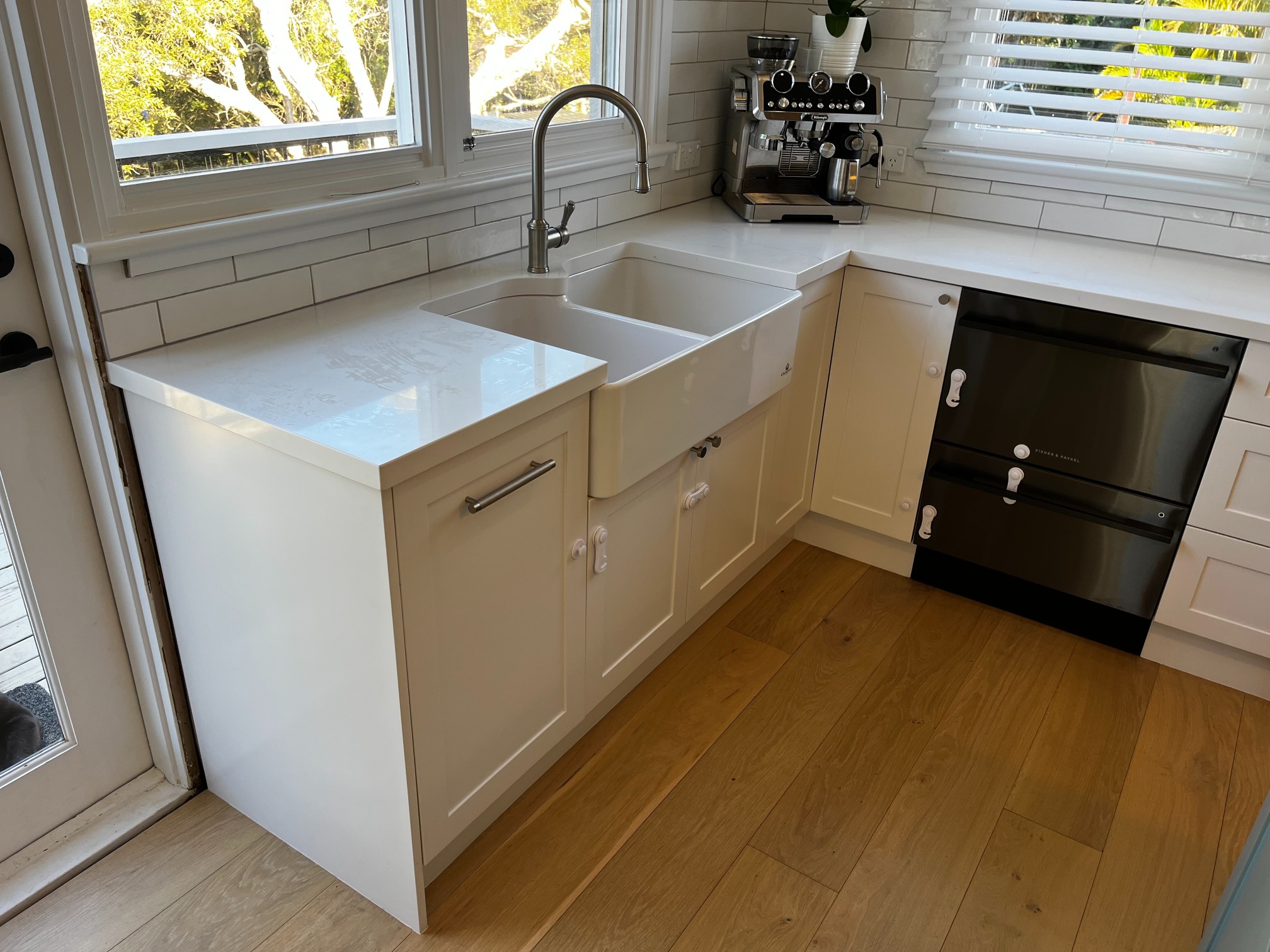 White kitchen by Red Hot Kitchens with farmhouse sink, double oven, espresso machine, custom cabinetry & sunlight.