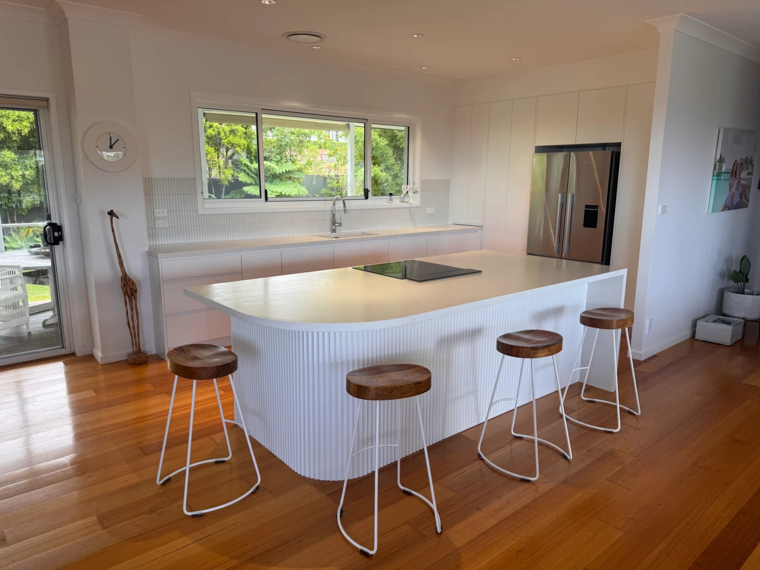 Allambie Heights kitchen with a curved white island, fluted breakfast bar, four stools and timber flooring.