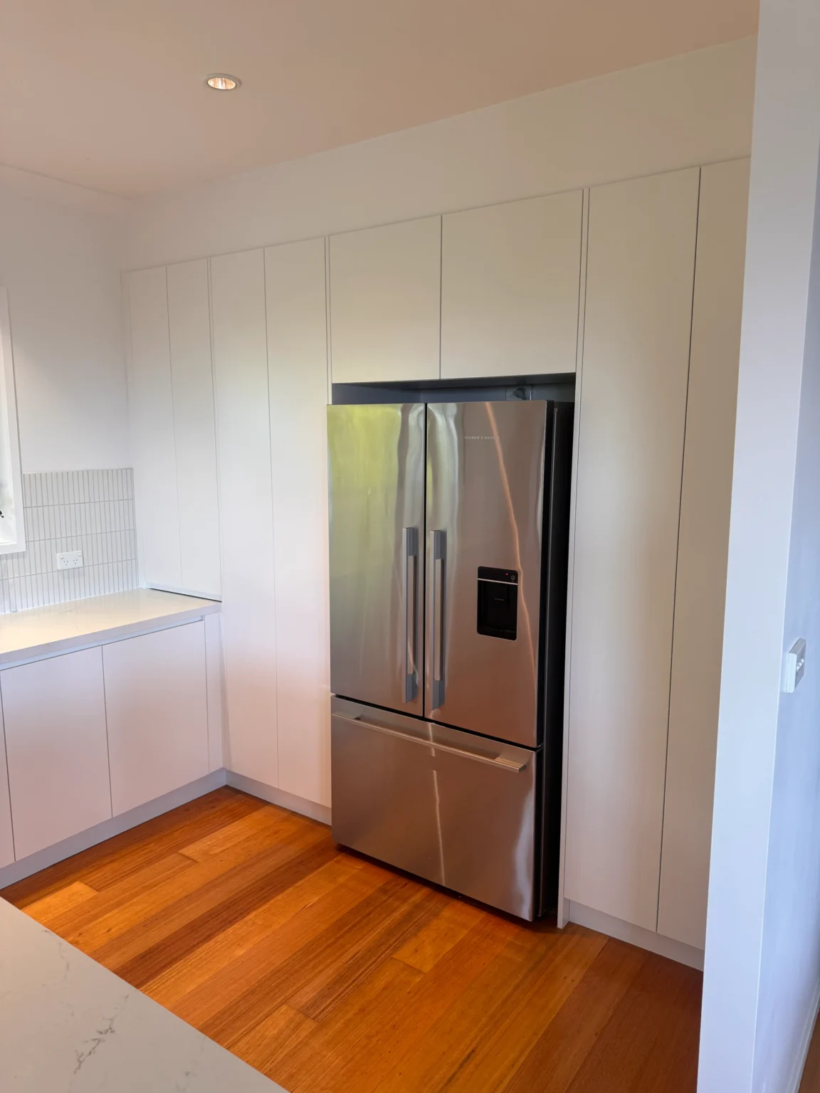 Full-height white kitchen cabinetry surrounding a stainless-steel fridge beside a window in Allambie Heights.