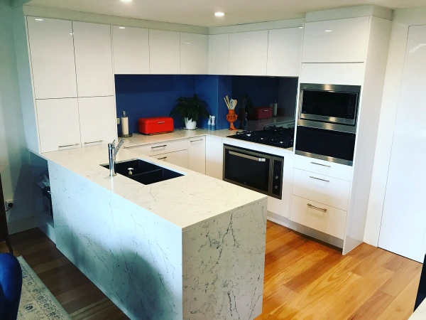 Renovated Brookvale kitchen with glossy white cabinetry, dark splashback and marble-look peninsula