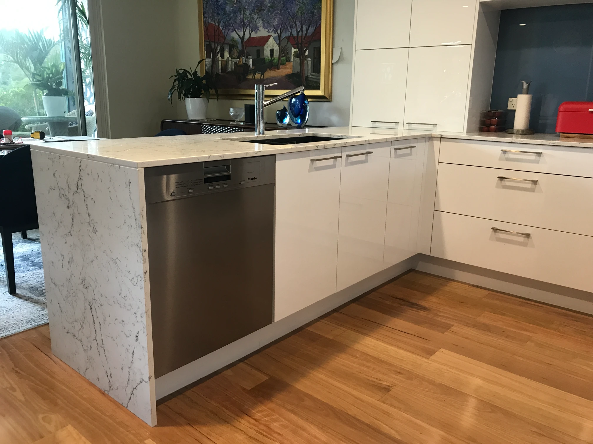 Brookvale kitchen with a marble-look waterfall peninsula, black inset sink, stainless-steel dishwasher and white cabinetry.