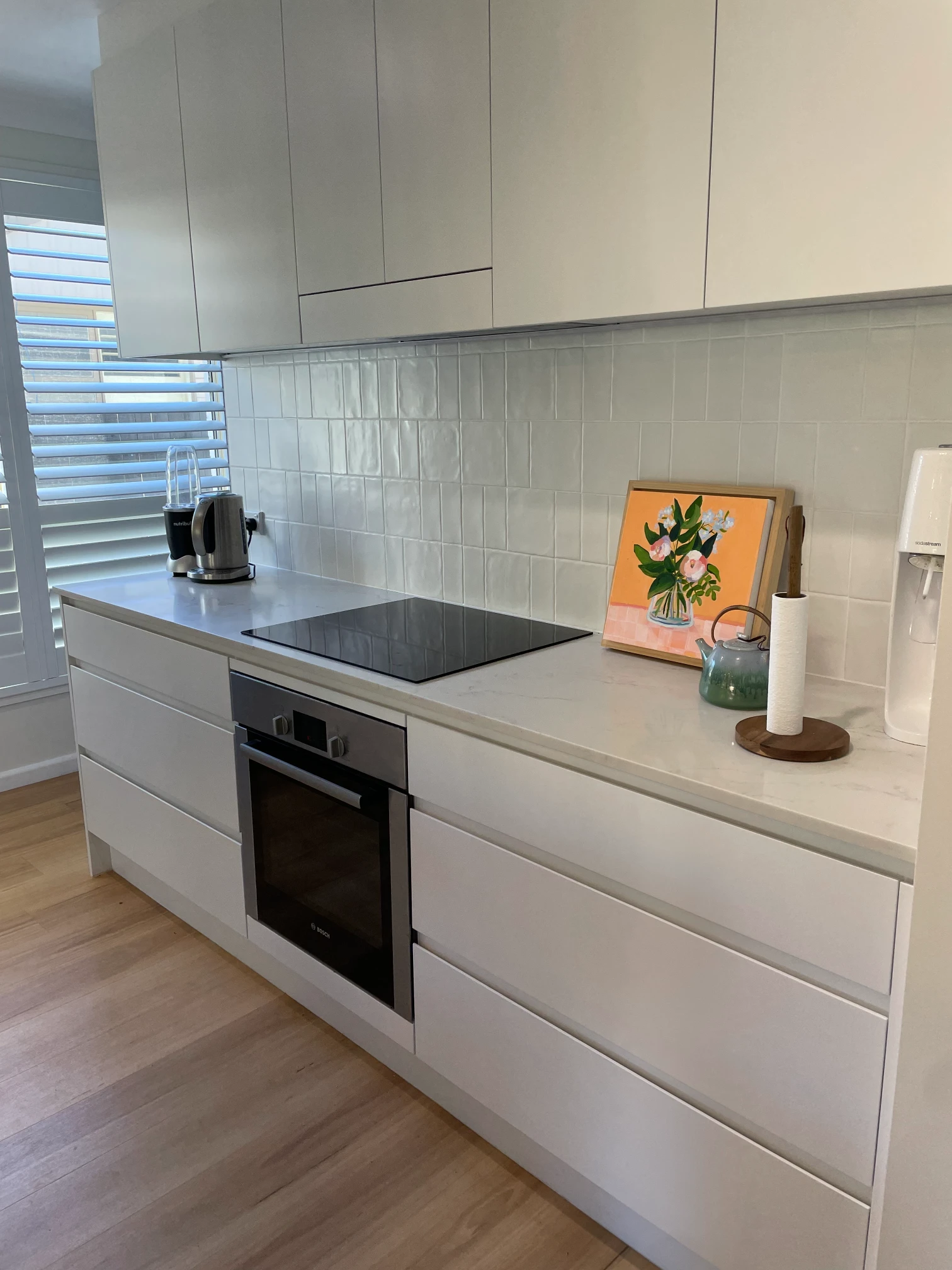 Black cooktop and built-in oven surrounded by white drawers, overhead cupboards and a white tiled splashback in Cromer.