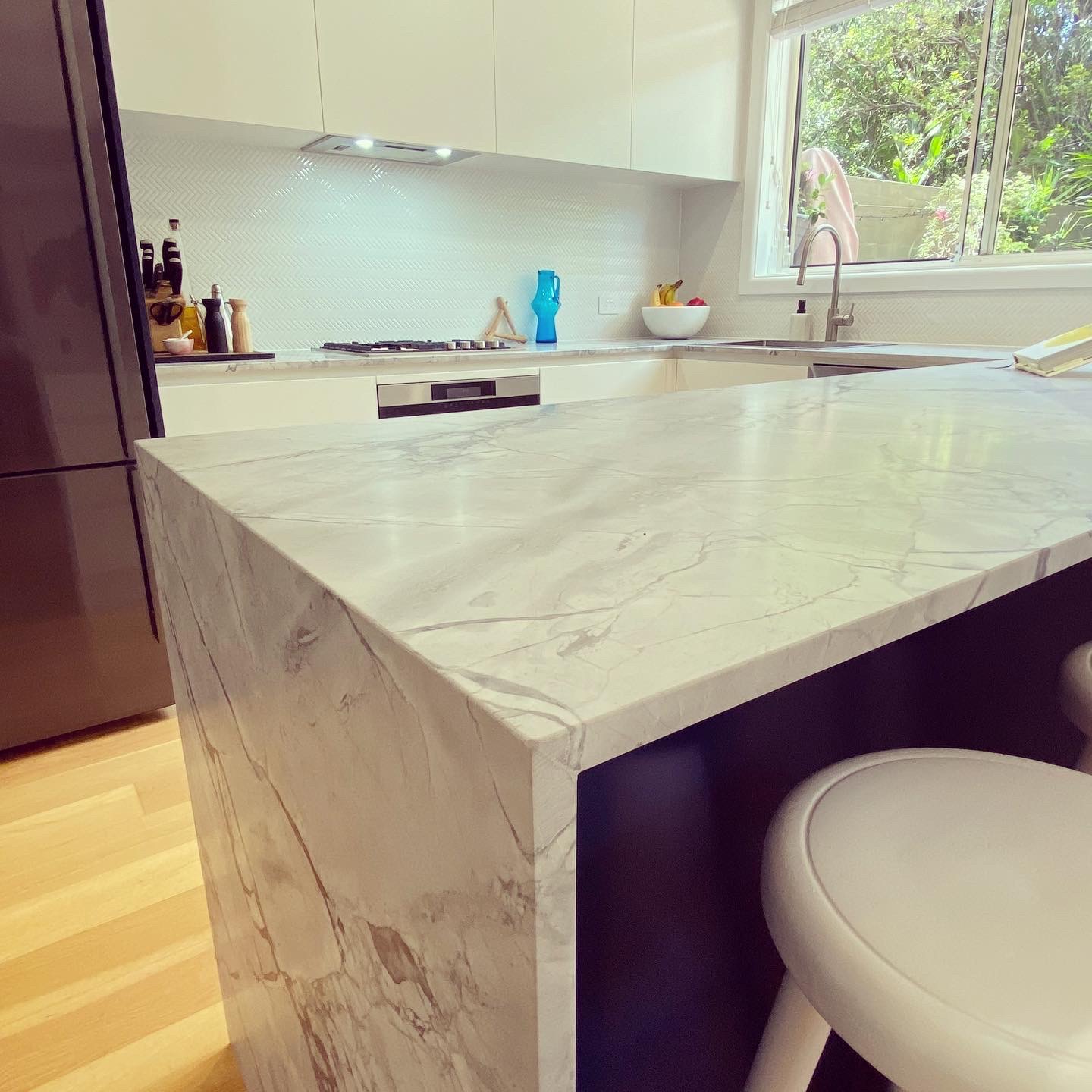Modern kitchen renovation in Dee Why with a large marble island featuring waterfall edges and white cabinet storage.