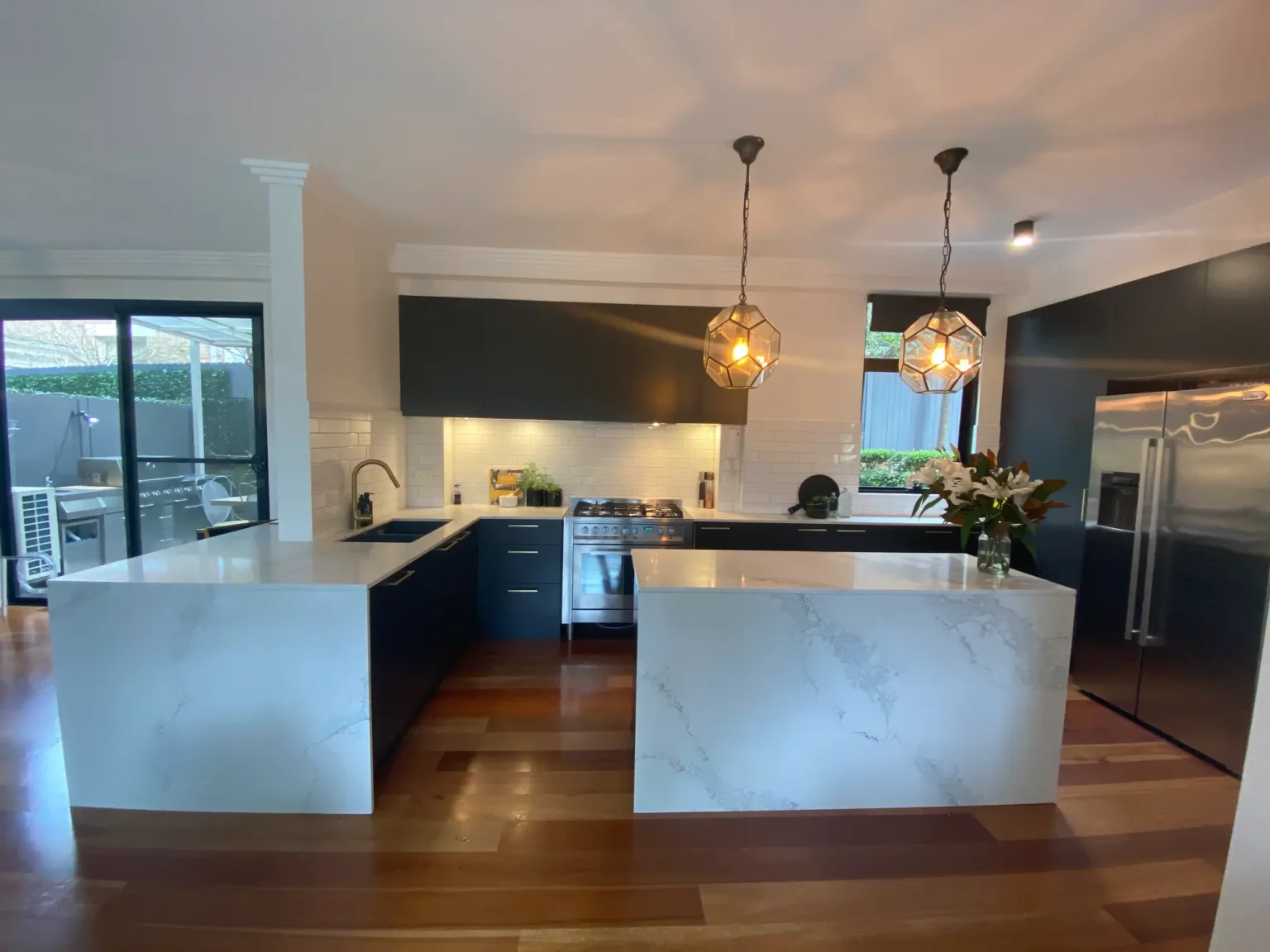 Modern kitchen renovation in Dee Why featuring dark cabinets, white marble island, and geometric pendant lights.