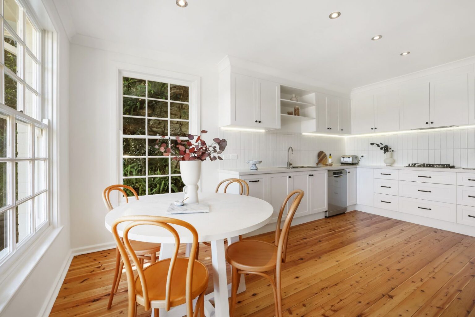 Bright white kitchen in Freshwater with a large window, timber floors and a round dining table