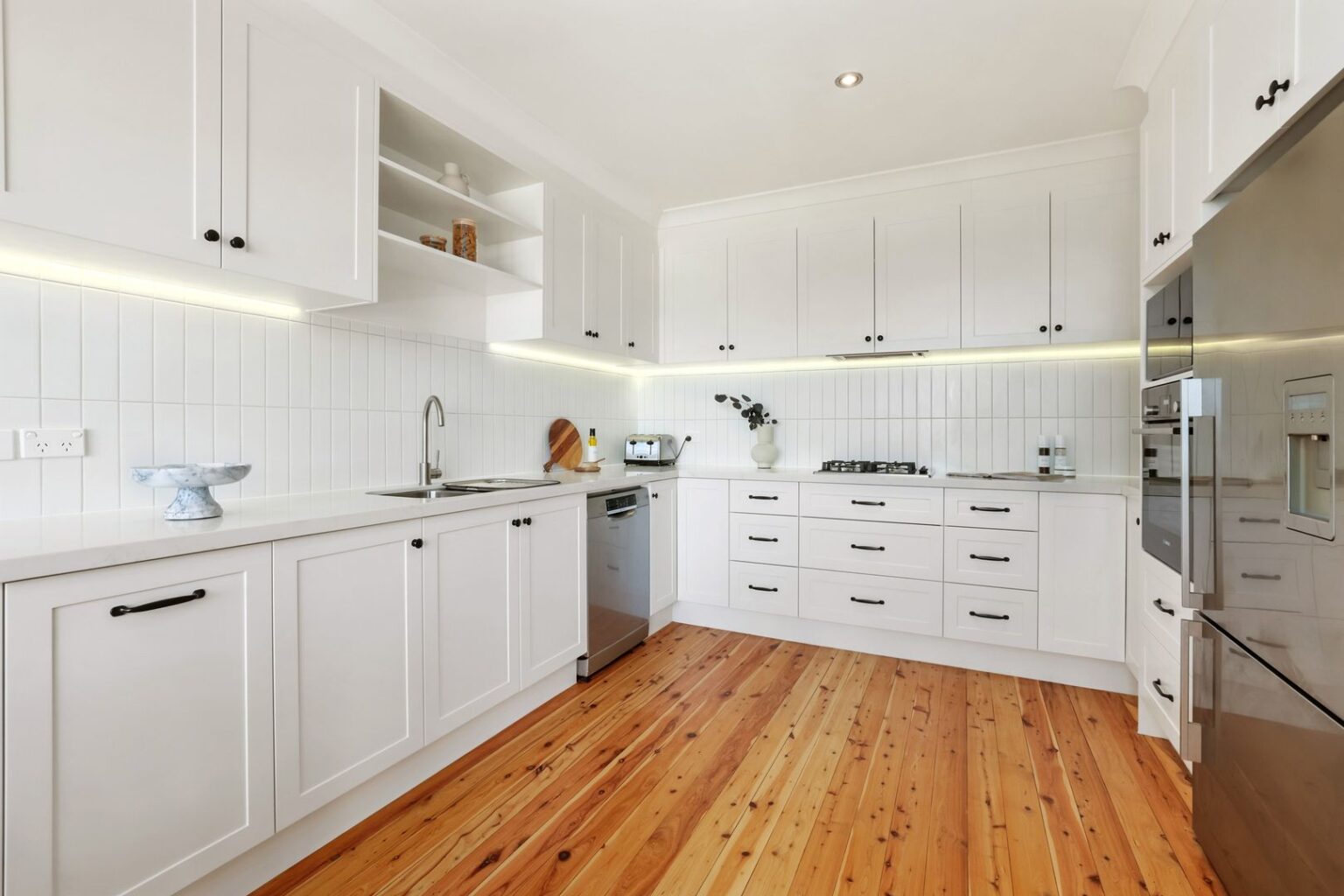 White kitchen in Freshwater with under-cabinet lighting, vertical-groove splashback and gas cooktop