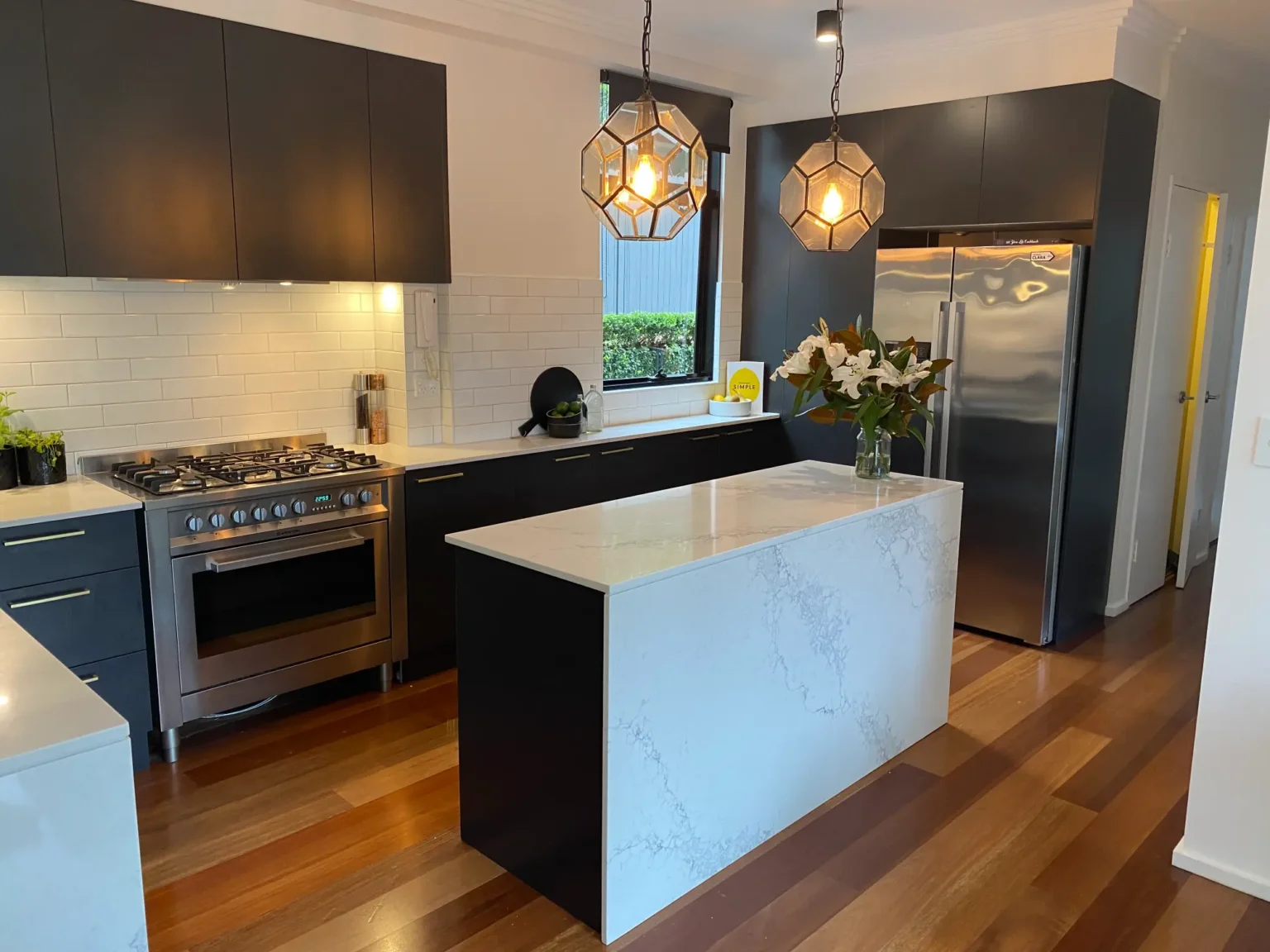 Modern full kitchen renovation in Dee Why showcasing elegant dark cabinetry, a marble-topped island, and a stove.