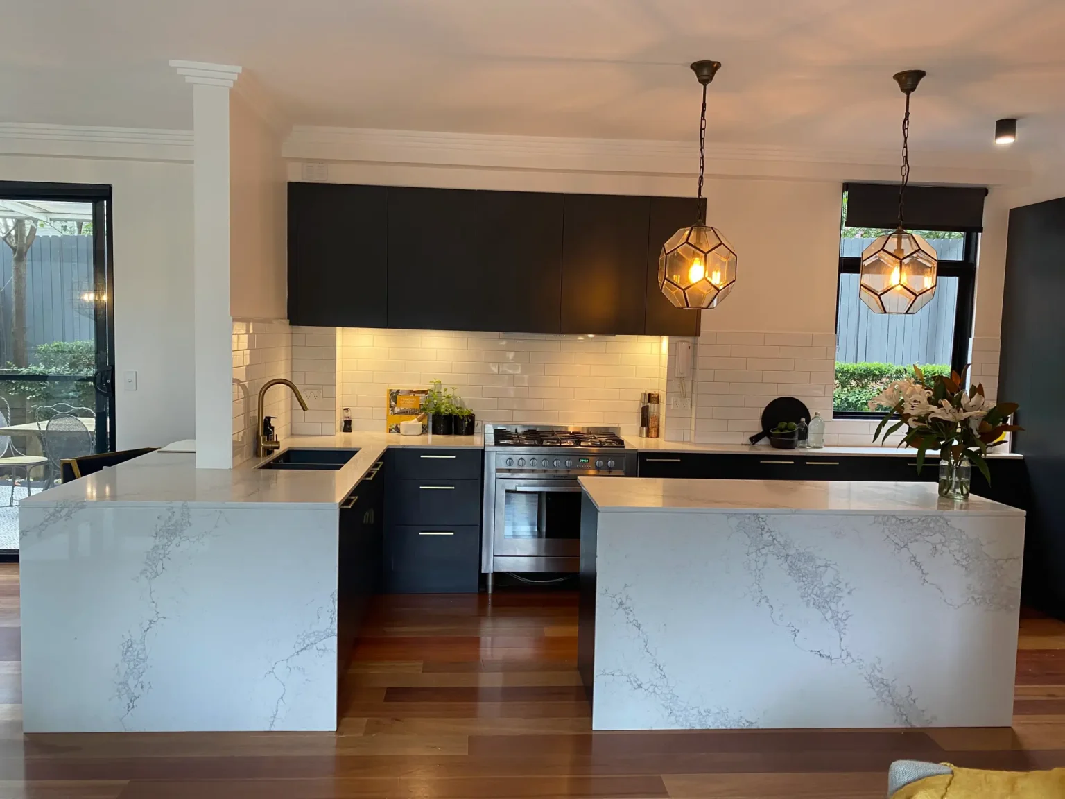 Modern kitchen renovation in Dee Why featuring dark cabinets, white stone countertops, and stylish pendant lights.