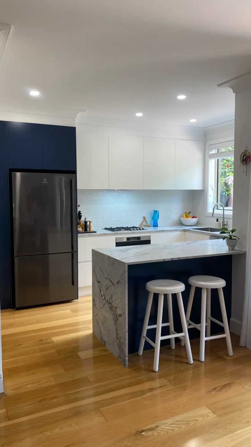 Modern kitchen renovation in Dee Why featuring navy and white cabinets, stainless fridge, and a marble island.