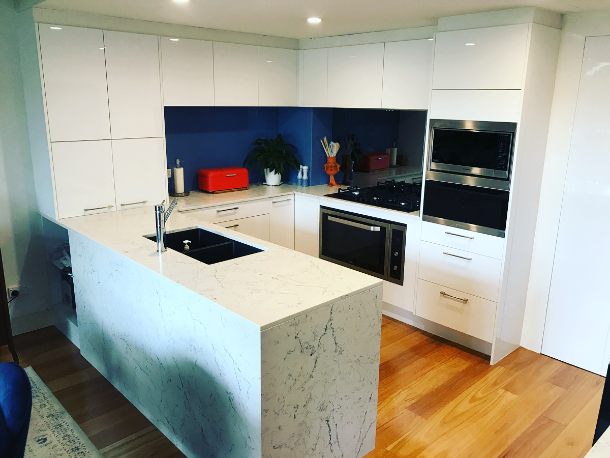 Renovated kitchen by Red Hot Kitchens with white cabinets, stone island, black sink, and bold blue splashback.