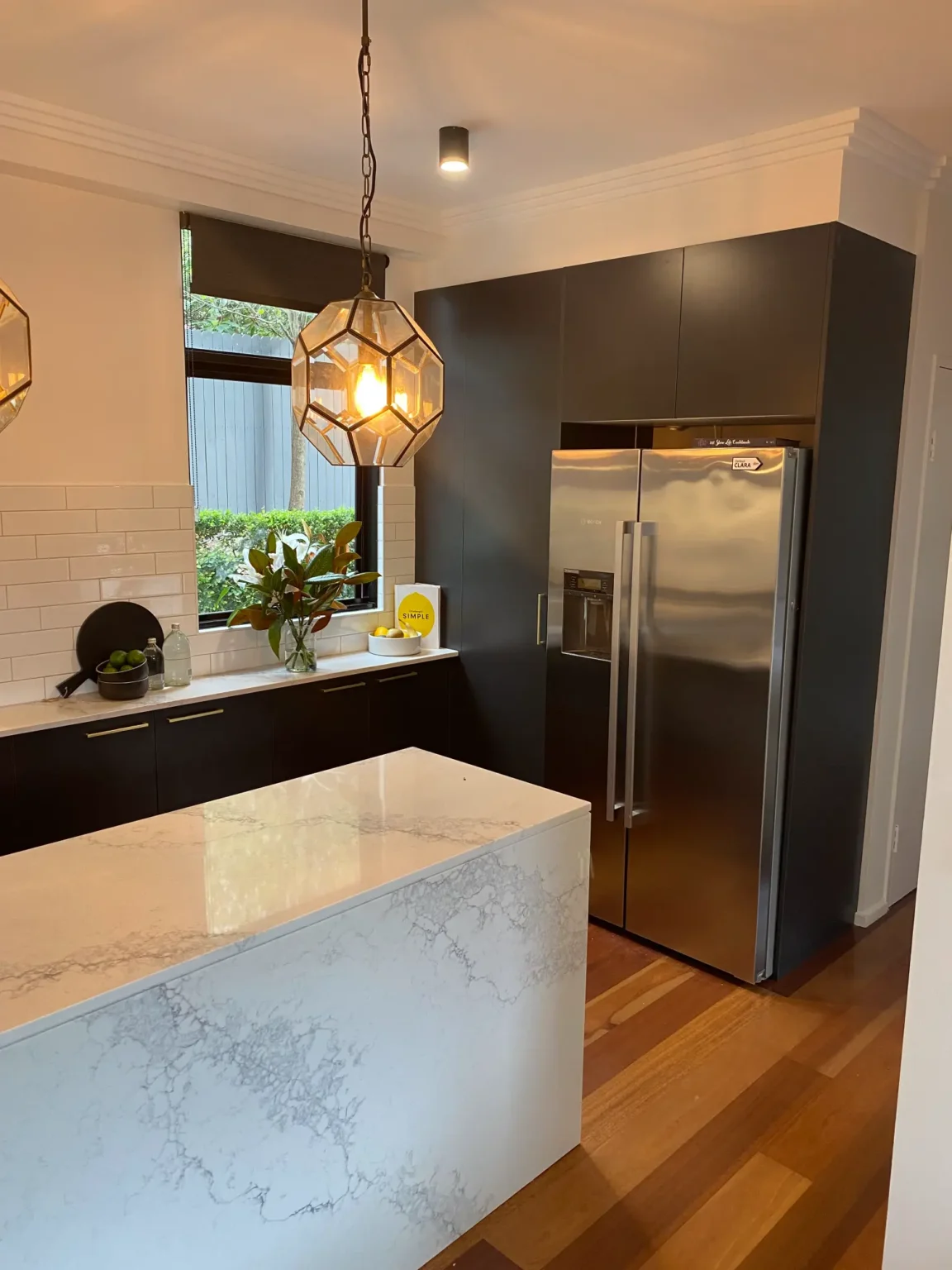 Modern kitchen renovation in Dee Why with white marble island, dark cabinetry, and stainless steel fridge design.