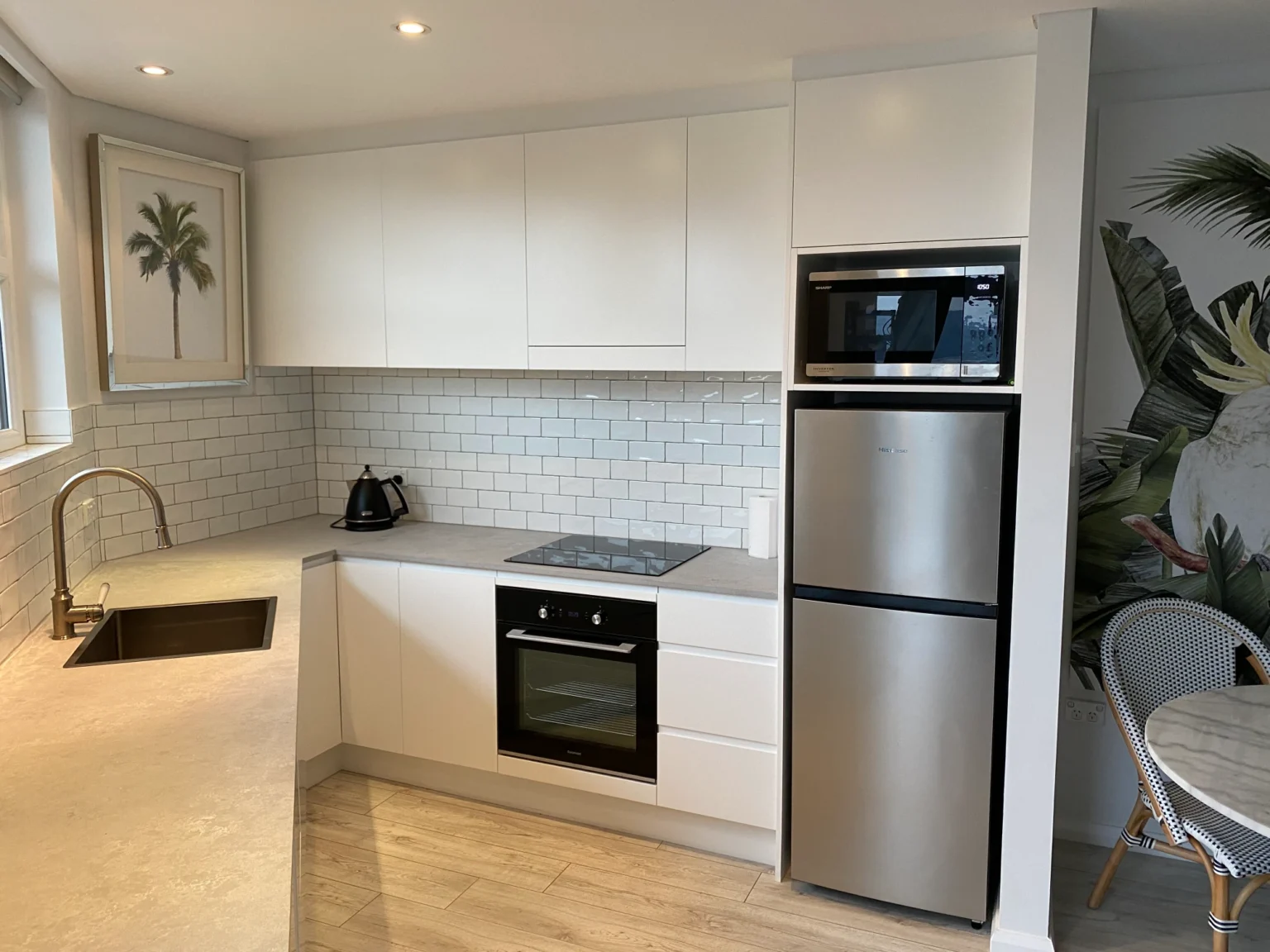 Modern apartment kitchen renovation with white cabinets, stainless steel fridge, built-in oven, and subway tile.