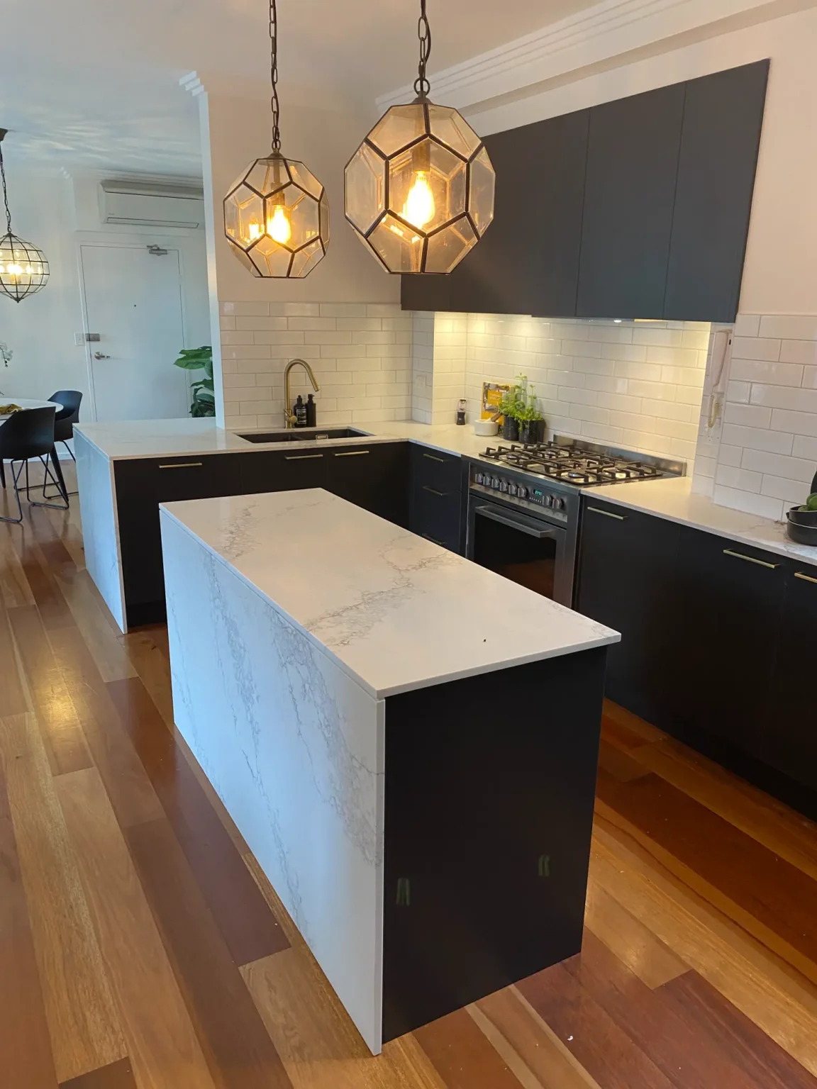 Modern kitchen renovation in Dee Why with sleek black cabinets, white marble island, and unique geometric lighting.