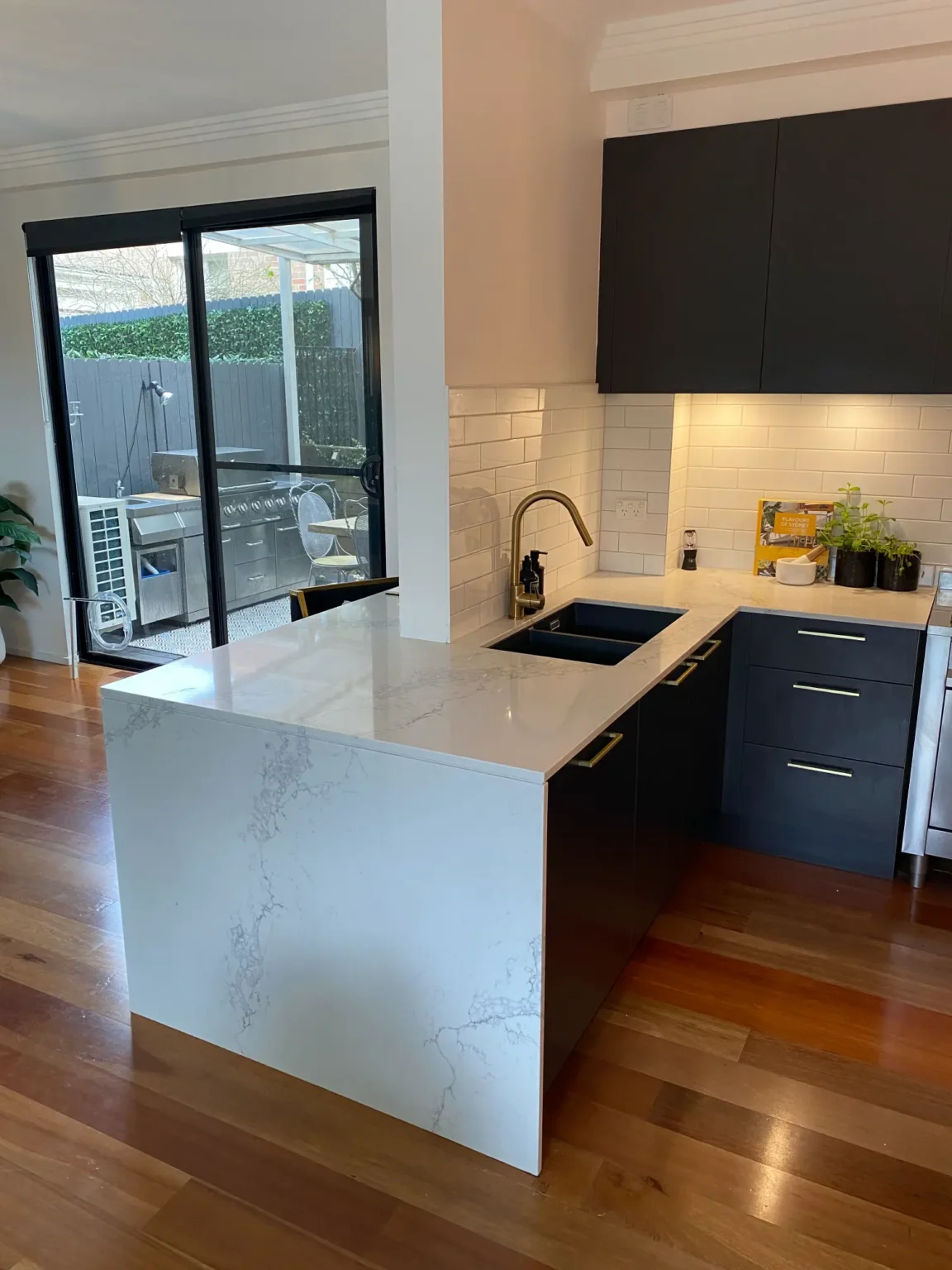Modern kitchen with dark cabinets, white marble island, and gold fixtures for a full renovation in Dee Why home.