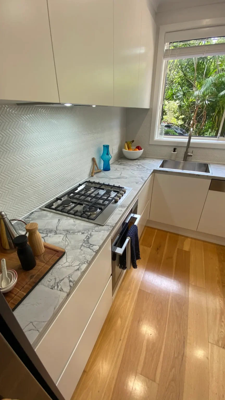 Modern white kitchen renovation in Dee Why featuring marble countertops, a gas cooktop, and beautiful timber floors.