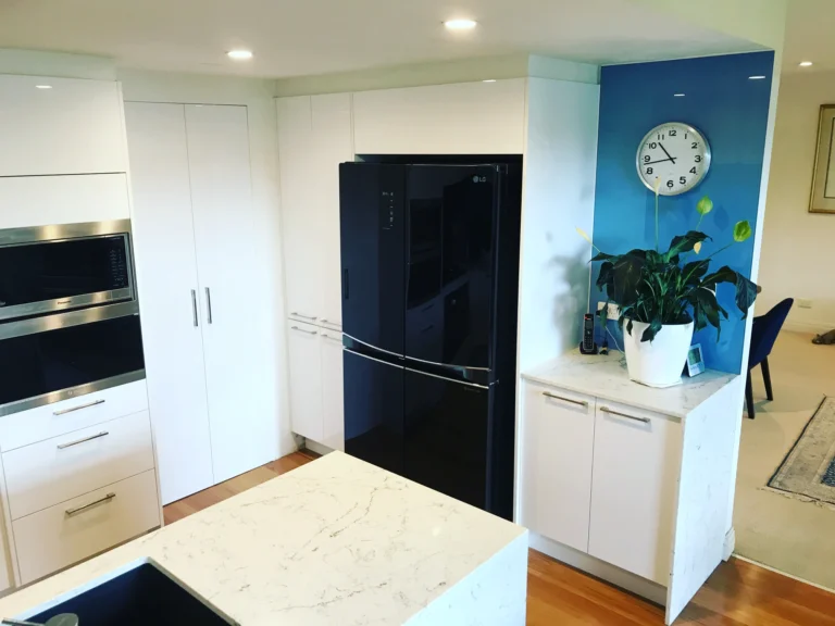 Modern white kitchen by Red hot kitchens in Brookvale, featuring a black refrigerator, blue accent wall and clock.
